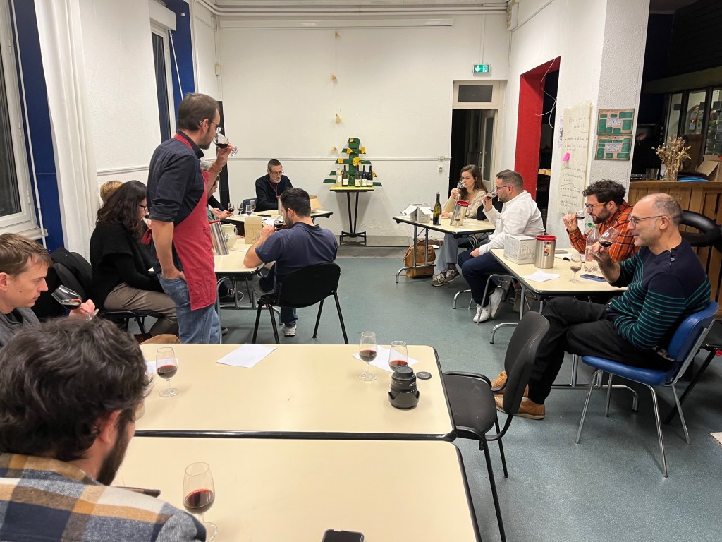 Participants attablés dans une salle pendant une dégustation de Noël, Jeremy Debreu debout au fond