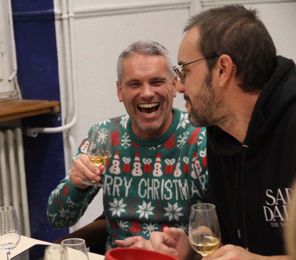 Deux collègues qui rient, un verre de vin à la main, l’un en pull de Noël